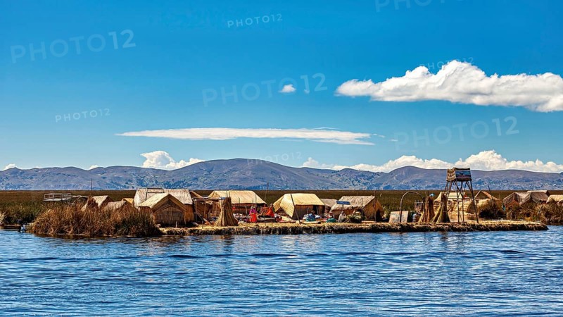 Reed huts on an island in the lake under a clear sky with mountains in the background, The floating reed islands of the Uros in Lake Titicaca in Peru