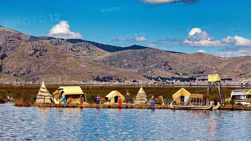 People and reed huts on the shore of a lake with mountains in the background under a clear sky, The floating reed islands of the Uros in Lake Titicaca in Peru