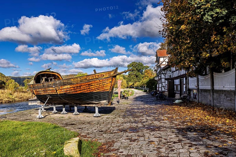 Rustic wooden boat on supports on a paved road next to a half-timbered house in autumn, the port of Wanfried an der Werra with the historic Werra ship