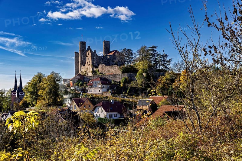 Castle above a village with a church, surrounded by autumn trees under a blue sky, Hanstein Castle near Bornhagen in the Eichsfeld district of Thuringia