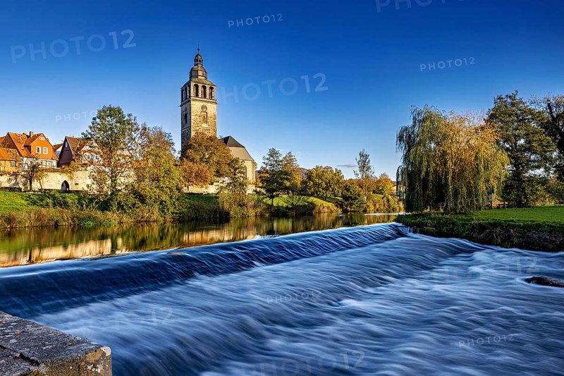 A church on the river with a small waterfall in the foreground and autumn trees in the background, the town of Bad Sooden Allendorf an der Werra in the Werra Meissner district of Hesse