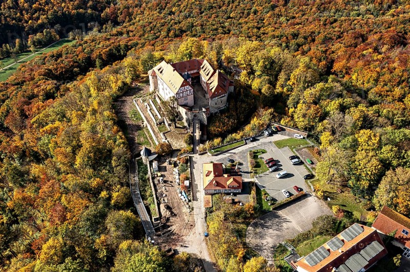 Aerial view of a castle in the autumn landscape with adjacent parking lot, surrounded by colorful trees, Bodenstein Castle in the Eichsfeld district of Thuringia