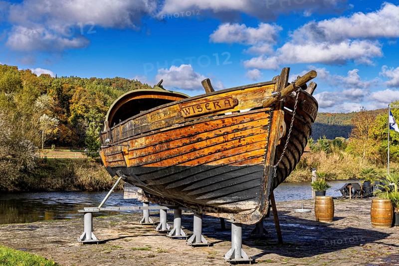 Historic wooden boat on the riverbank on supports, surrounded by autumn trees under a blue sky, the port of Wanfried an der Werra with the historic Werra ship