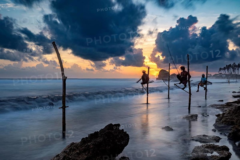 Silhouette of fishermen at sunset over the blue and orange sea, Koggala beach with stilt fishermen in Sri Lanka