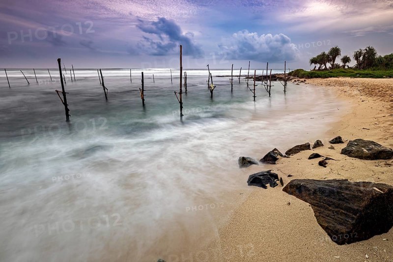 Dramatic sunset on the beach with stilts and waves, Koggala beach with stilt fishermen in Sri Lanka
