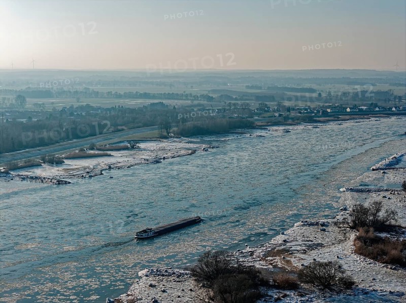 On a cold winter day, a barge sails downstream on the Elbe near Hamburg when there is slight ice. The foothills of the Elbe are icy in the flooded area. Kirchwerder, Hamburg, Germany