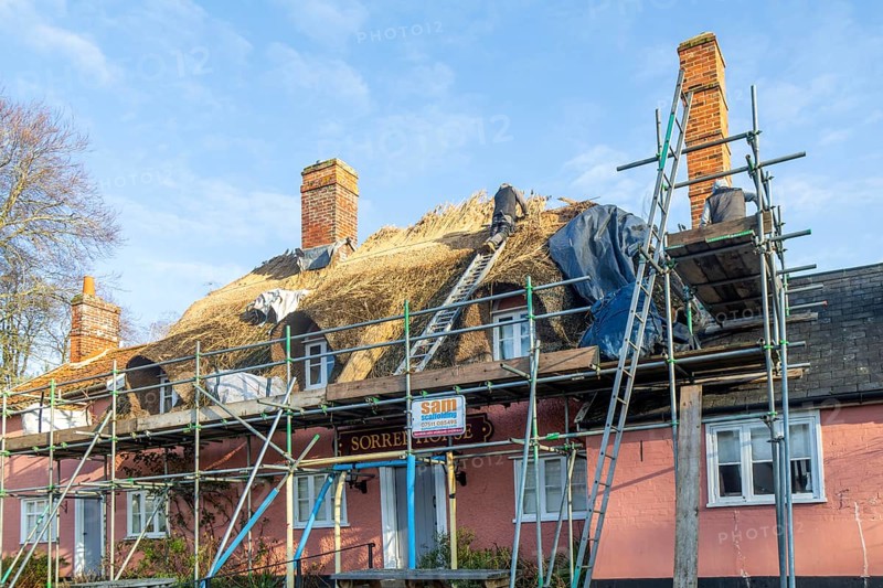 Thatcher at work replacing thatch ridge of thatched country pub building, Sorrel Horse, Shottisham, Suffolk, England, UK