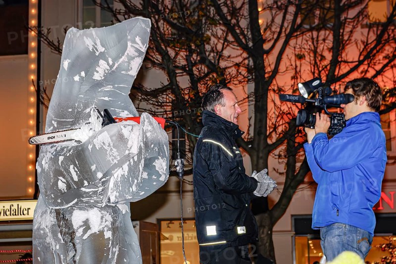Ice carving artist in front of his ice sculpture interviewed by a GEA reporter during ice carving street action as part of the long shopping night in downtown Reutlingen, Baden-Württemberg, Germany, for editorial use only