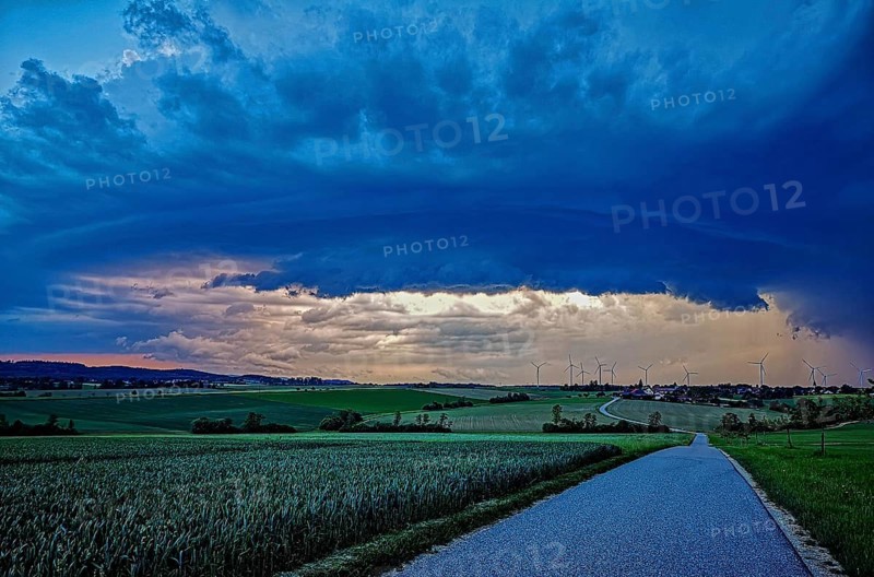 Supercell, approaching thunderstorm with impressive and threatening cloud formation, a thunderstorm over a country road and a village with wind turbines in the background, Baden-Württemberg, Germany