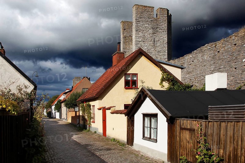 Alley with traditional half-timbered houses and towers of the city wall in Visby under threatening clouds, Visby, Gotland, Sweden