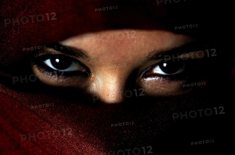 Mysterious eyes peek out from under a red veil