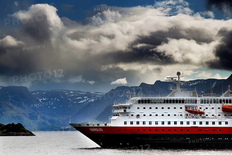 A Hurtigruten ship against a dramatic backdrop of clouds in Øksfjord, Øksfjord, Norway