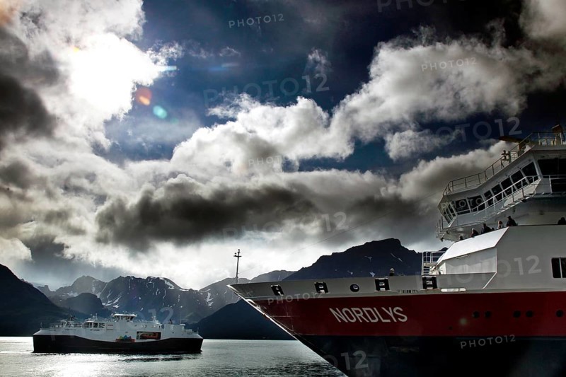 Hurtigruten ship near Øksfjord against dramatic sky and mountains, Øksfjord, Norway
