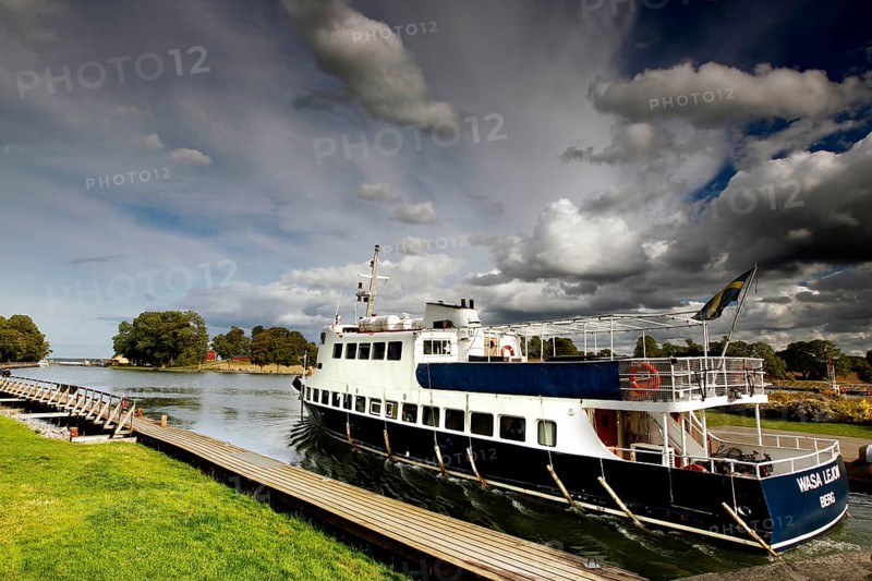 Passenger ship in the Göta Canal at a dock under a cloudy sky, mountain, Sweden