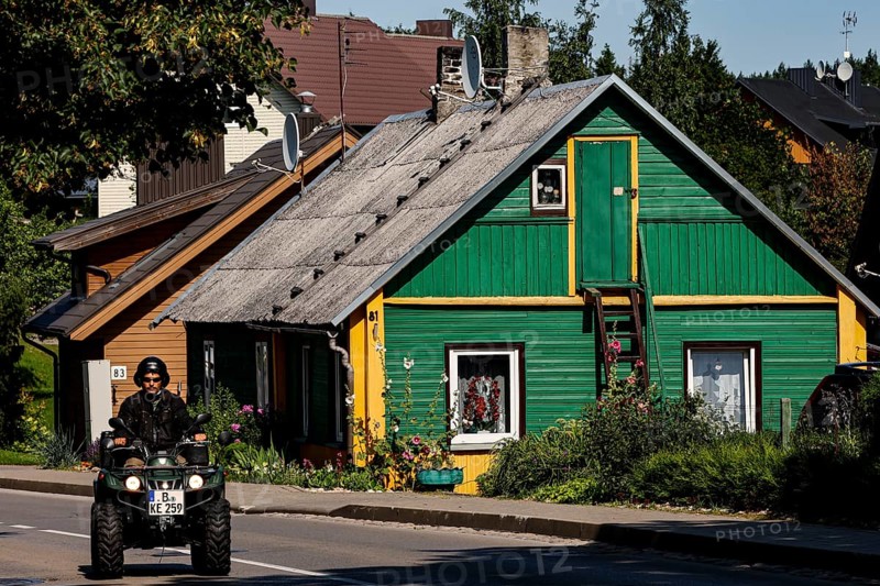 Green wooden house in Trakai with a passing ATV on the road in front of it, Trakai, Lithuania