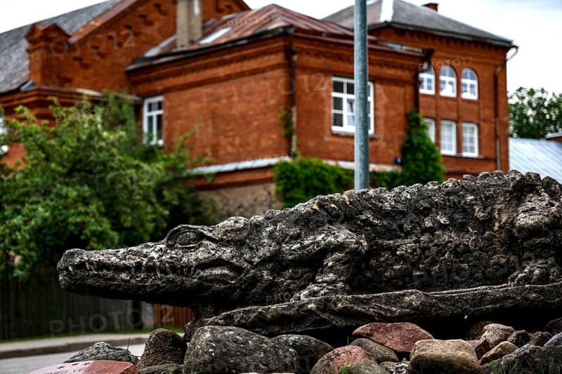 Crocodile sculpture in front of a historic brick building in green surroundings, Dundaga, Latvia