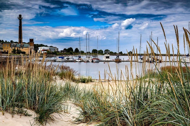 View of beach and harbor with boats and lighthouse in sandy dune landscape, Engure, Latvia