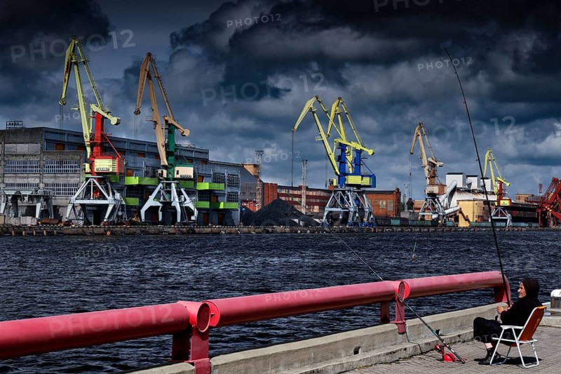 Harbour with cranes and an angler in the foreground under cloudy sky, Ventspils, Latvia