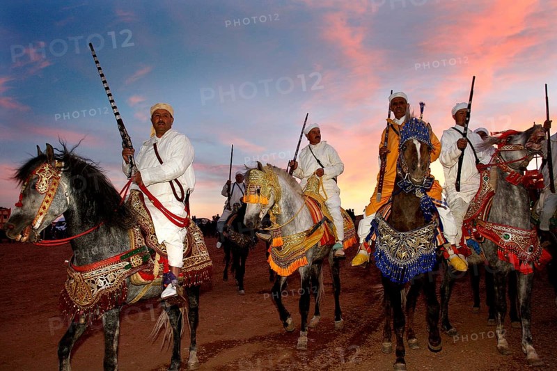 Riders wearing traditional clothes at sunset during a Fantasia performance, El Kelâa m'Gouna, Morocco