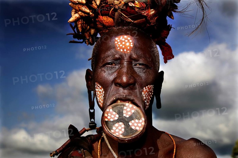 Mursi woman with lip plate and traditional headdress under dramatic sky, Mago National Park, Ethiopia