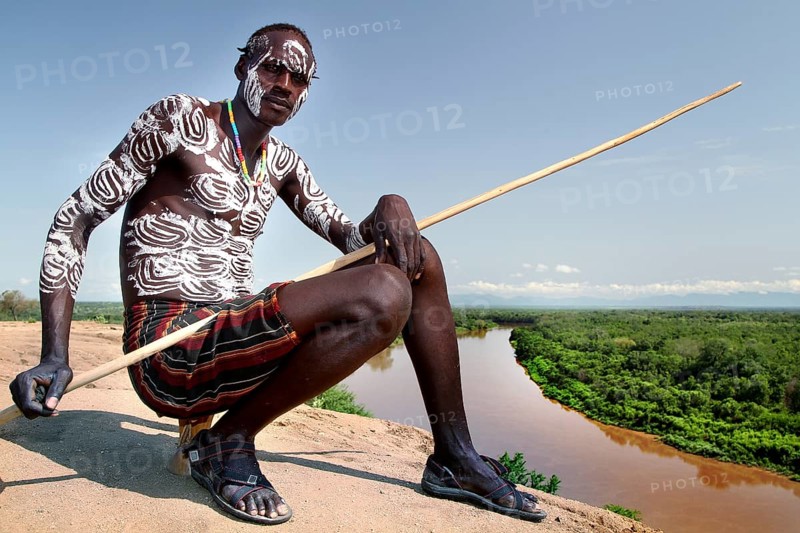 Oytade sitting with a spear, overlooking the river in the village of Murle, Murle, Ethiopia