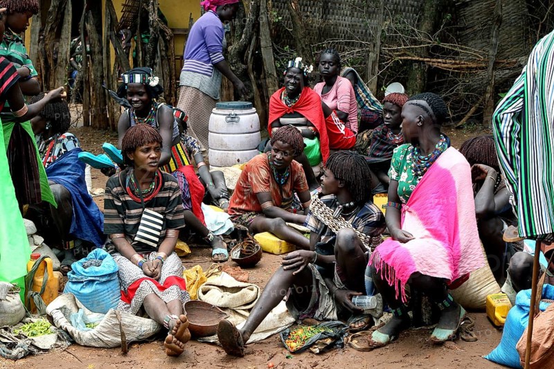 People in colorful clothes sit at a market and exchange goods