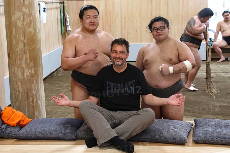 Man sitting smiling in front of two sumo wrestlers at Ryogoku training center, Tokyo, Ryogoku, Japan