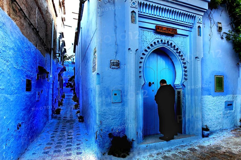 Blue alley with traditional Moroccan gate and a person in the medina of Chefchaouen, Chefchaouen, Tanger-Tetouan, Morocco