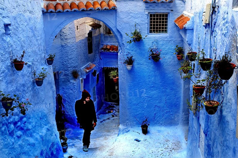 Blue alley with arches and flower pots interspersed with a passing person in the Medina, Chefchaouen, Tanger-Tetouan, Morocco