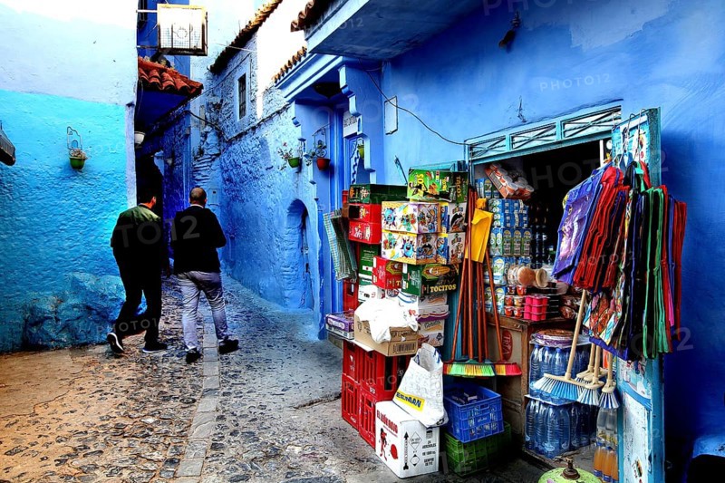 Market stand on a blue wall in the medina of Chefchaouen, people strolling, Chefchaouen, Morocco