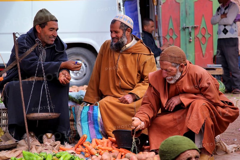 Men wearing traditional clothes at a market in Achaouikh, engaged in conversation, zero