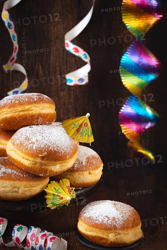 A pile of donuts with powdered sugar, colorful garlands and streamers against a dark wooden background, carnival