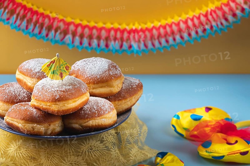 A plate of donuts with powdered sugar on a table surrounded by colorful carnival decoration
