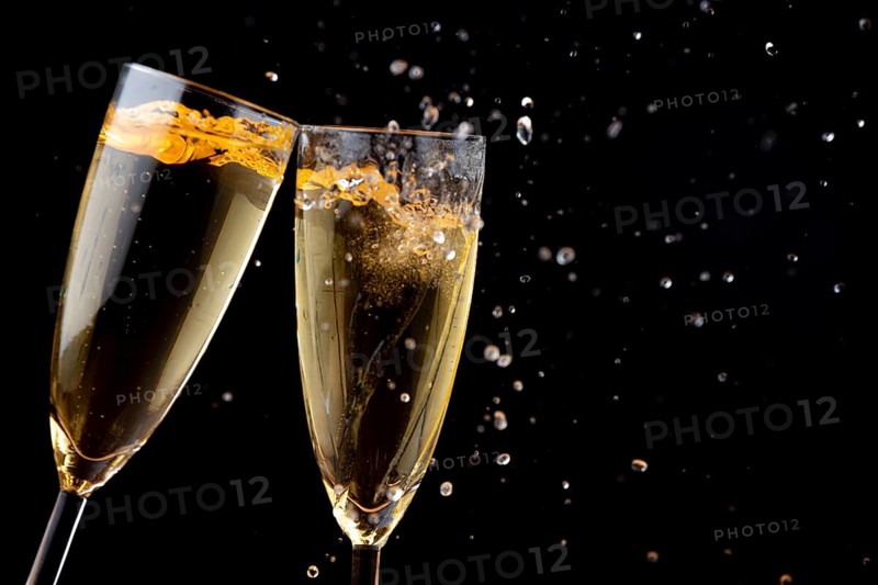 Two glasses of champagne touching each other with splashes against a dark background
