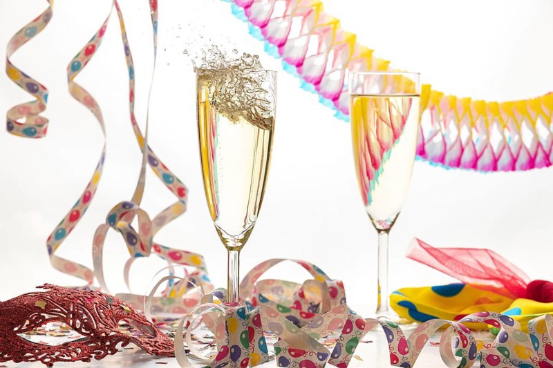 Two champagne glasses, one sparkling, in a lively atmosphere with streamers and a mask, carnival