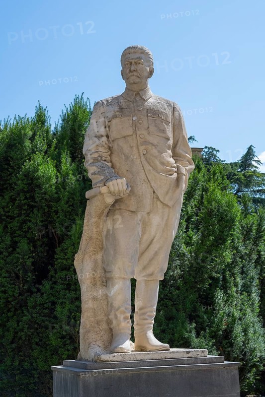 Stone statue of a man in uniform in front of a green hedge outdoors, Stalin monument, sculpture, Gori, Inner Kartli region, Georgia