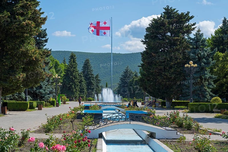 Parkland with central fountain surrounded by flowers and tall trees, Georgian flag, Stalin Park, Gori, Inner Kartli region, Georgia