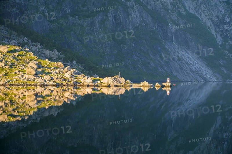 Sunny rocky landscape reflected on the calm water surface of Lysefjord, calm water reflects rocks and stones under a blue sky, Lysefjord, Rogaland, Norway