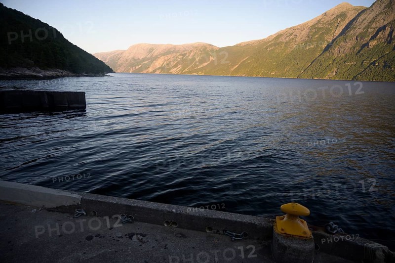 Songesand, Rogaland Municipality, Norway, coastline with calm water and shade on mountains at dusk