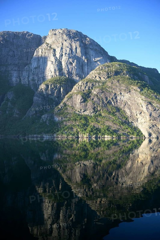 Majestic rocks reflected in clear water under a bright blue sky at Lysefjord, Rogaland, Norway