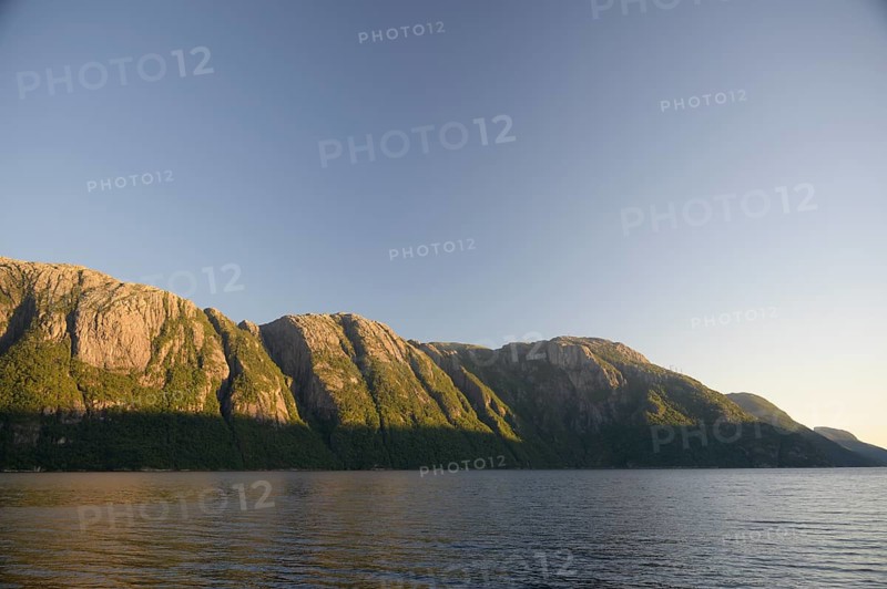 Rocky mountain range along a body of water under clear sky at Lysefjord at sunrise, Lysefjord, Rogaland, Norway
