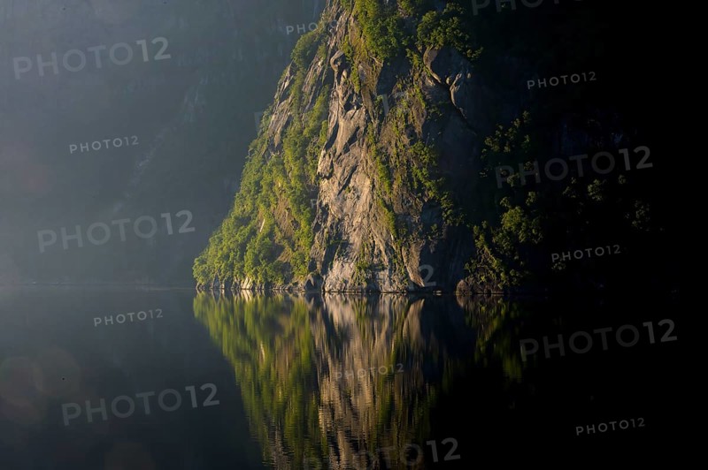 A steep rock rises up, its massive presence reflected in still water, Lysefjord, Rogaland, Norway