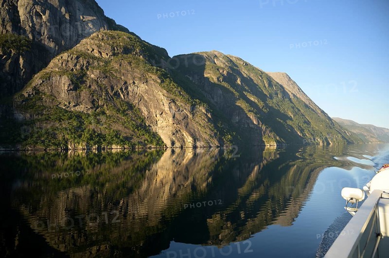 A boat sails along an orderly and peaceful Lysefjord surrounded by massive rock walls, Lysefjord, Rogaland, Norway