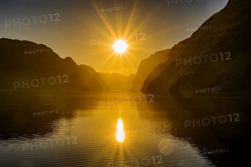 Atmospheric star-shaped sunlight is reflected on quiet fjord waters of Laysefjord between massive rock walls, view from Columbus ferry, Lysefjord, Rogaland, Norway