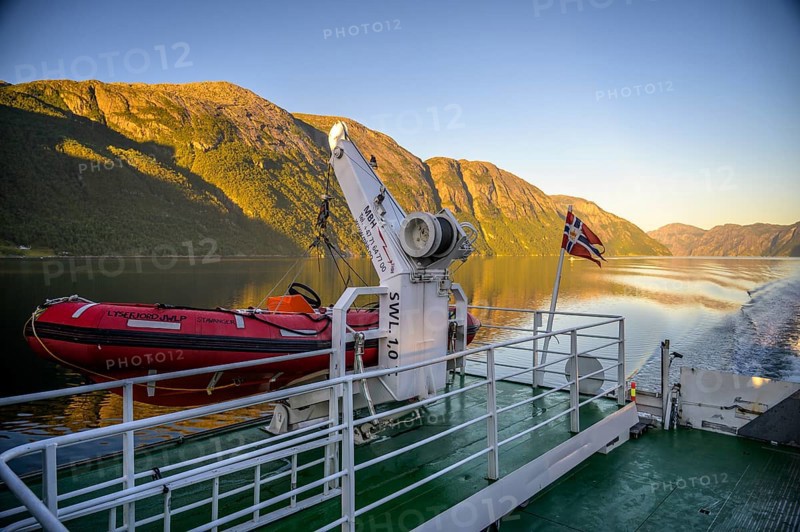 Red lifeboat and Norwegian flag on a ferry in the Lysefjord at sunset, view from the Columbus ferry, Lysefjord, Rogaland, Norway
