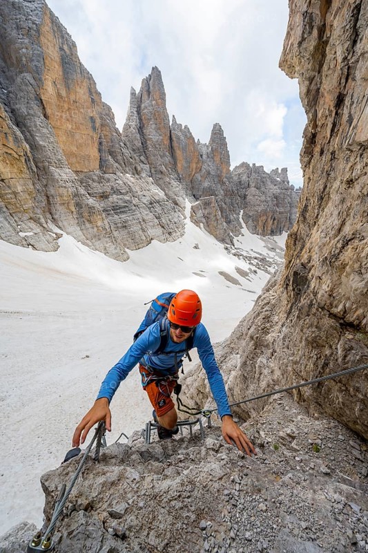 Mountaineer climbs on a steep rock face in the Via Ferrata dell'Ideale via ferrata, spectacular mountain landscape with steep rock faces, remnants of the Vedretta d'Ambiez glacier in the back, Brenta Mountains, Brenta-Adamello Nature Park, Trentino, Italy