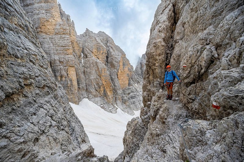 Mountaineer climbs on a steep rock face in the Via Ferrata dell'Ideale via ferrata, spectacular mountain landscape with steep rock faces at the Bocca d'Ambiez, remnants of the Vedretta d'Ambiez glacier, Brenta Mountains, Parco Naturale Brenta-Adamello, Trentino, Italy