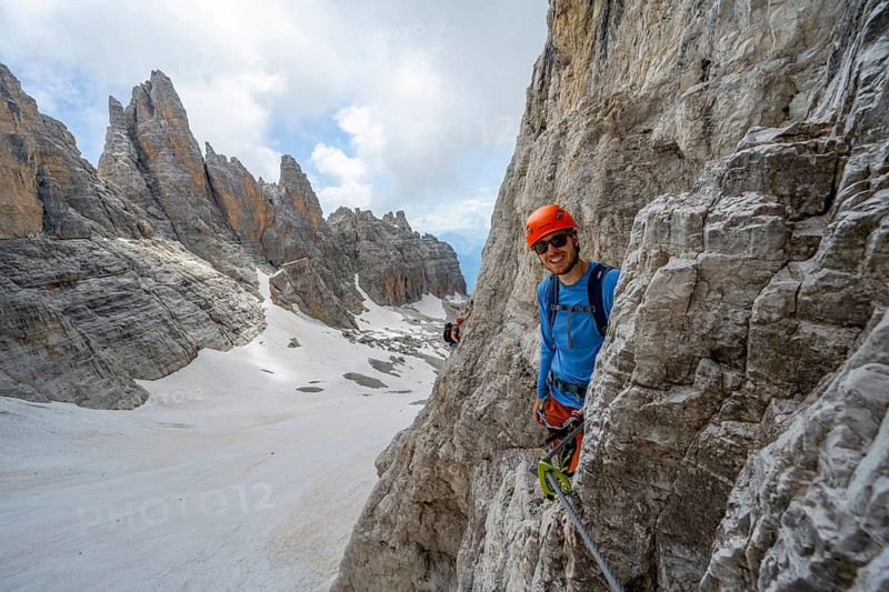 Mountaineer climbs on a steep rock face in the Via Ferrata dell'Ideale via ferrata, spectacular mountain landscape with steep rock faces, remnants of the Vedretta d'Ambiez glacier in the back, Brenta Mountains, Brenta-Adamello Nature Park, Trentino, Italy