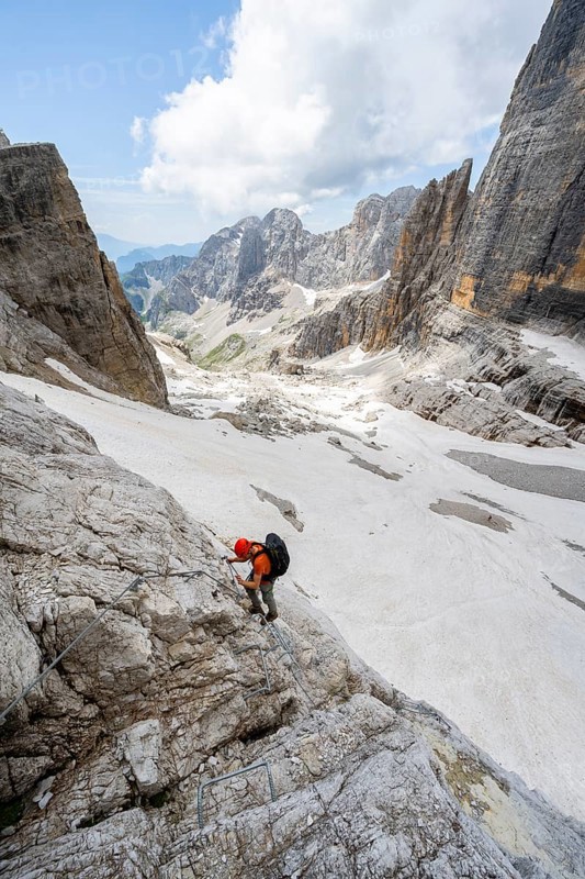 Mountaineer climbs on a steep rock face in the Via Ferrata Brentari via ferrata, spectacular mountain landscape with steep rock faces, remains of the Vedretta d'Ambiez glacier in the back, Brenta Mountains, Brenta-Adamello Nature Park, Trentino, Italy
