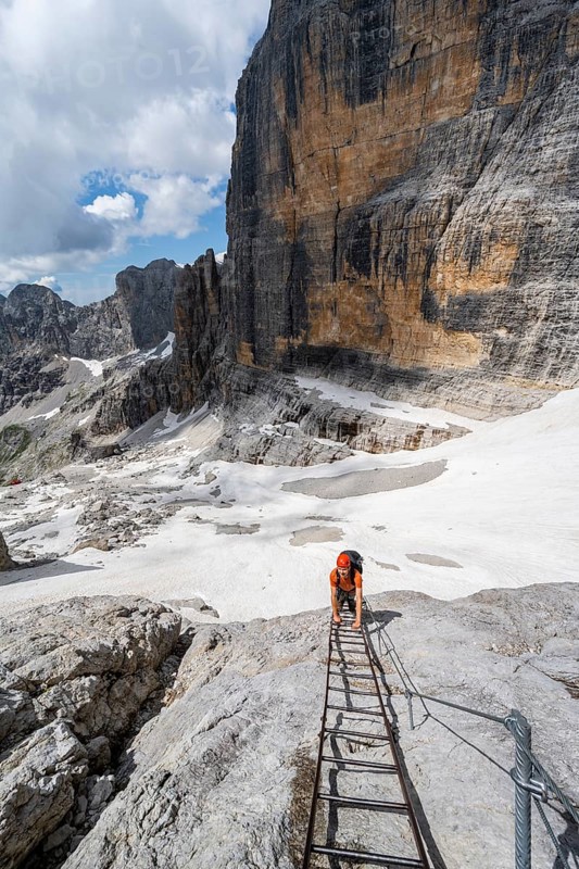 Mountaineer climbs on a ladder in the Via Ferrata Brentari via ferrata, spectacular mountain landscape with steep rock faces, remains of the Vedretta d'Ambiez glacier in the back, Brenta Mountains, Brenta-Adamello Nature Park, Trentino, Italy